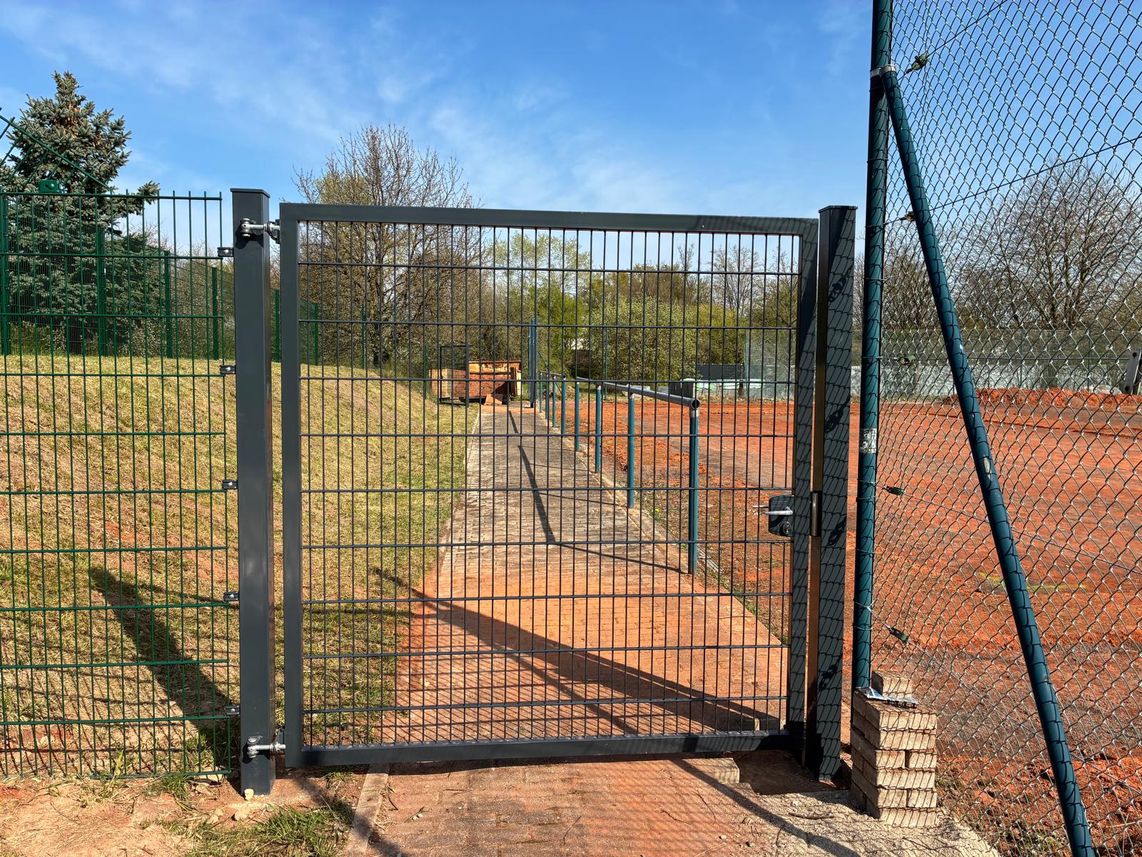 Gezeigt wird der ehemalige Tennisplatz mit einem neuen zaun und einem neuen Eingangsbereich